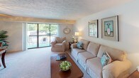 Located at 28241 Center Ridge Rd in Westlake, Ohio, this single-floor residence offers a comfortable and thoughtfully laid-out living space. The living room serves as the heart of the home, featuring plush carpeting, warm ambient lighting, and a large sliding glass door that opens to a private outdoor patio with views of mature greenery, filling the room with natural light. Adjacent to the living room, the dining area provides an intimate setting highlighted by a ceiling fan with light fixture and chair-rail wall detailing. The galley-style kitchen is well-equipped with warm wood cabinetry, dark granite-style countertops, a double sink, and white appliances including a range, built-in microwave, dishwasher, and refrigerator. The bedroom is a serene retreat with carpeted floors, a window dressed with elegant curtains, and ample space for furnishings. A versatile secondary room with carpeting and a window offers flexibility as a home office or additional sitting area. Two full bathrooms complete the layout, each featuring a vanity with wood cabinetry and a large mirror, with one including a shower-tub combination. Textured ceilings are a consistent design element throughout the space, contributing to its classic and cozy character.