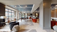 Located at 4015 Aspen Grove Dr in Franklin, Tennessee, this single-floor amenity clubroom is a masterfully designed communal space that blends contemporary sophistication with inviting comfort. The open-concept layout is anchored by a striking chevron-patterned floor in neutral tones, which flows seamlessly throughout the entire space and creates a bold visual foundation.

The room is divided into distinct functional zones without sacrificing its cohesive, open feel. A game area features a full-sized billiards table beneath a elegant chandelier, while floor-to-ceiling windows along the perimeter flood the space with abundant natural light and offer views of the surrounding streetscape. The lounge area centers around a sleek linear fireplace framed by a crisp white surround, complemented by richly upholstered seating in deep charcoal and vibrant burnt orange tones. Textured metallic wall panels and a dark coffered ceiling add depth and drama to this intimate seating zone.

Throughout the space, curated artwork, sculptural accent pieces, and bold geometric rugs contribute to a gallery-like atmosphere. Teal-painted coffered ceiling sections provide striking contrast against neutral walls, while recessed lighting ensures a warm, well-lit ambiance. Lush indoor plants add organic warmth, rounding out a space that is both visually dynamic and functionally versatile.