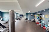 Located at 3695 General Parkway in College Station, Texas, this fitness center is a thoughtfully designed exercise facility spanning a generous single floor. The space is finished with a clean, modern aesthetic, featuring bold teal accent walls contrasted against crisp white ceilings and trim, creating an energizing atmosphere for workouts.

The facility is organized to accommodate a wide range of fitness activities. A dedicated cardio zone lines the perimeter, outfitted with treadmills, rowing machines, and stationary cycling bikes. Large windows and a set of glass double doors flood this area with natural light and offer pleasant outdoor views of the surrounding greenery. Reflective wall mirrors extend the visual depth of the space while supporting form-focused training.

The strength training area is well-appointed with a full dumbbell rack, a weight bench, a barbell squat rack, and multiple cable and resistance machines. Durable rubber flooring throughout provides safety and comfort underfoot. Overhead, linear LED lighting ensures bright, even illumination across the entire floor.

A standout feature is a large motivational mural reading "The Stronger You Are, The Better You Feel," adding character and energy to the space. The facility also includes a dedicated stretching and functional training zone with medicine balls and other accessories, making it a comprehensive and inviting environment for all fitness levels.