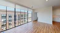 Located at 2922 W Marshall St in Richmond, VA, this 3-bedroom, single-floor unit offers a thoughtfully designed open-concept layout with modern finishes throughout. The combined kitchen and living area serves as the heart of the home, featuring warm hardwood-style flooring that extends seamlessly across the entire unit. The kitchen is appointed with sleek white cabinetry, contrasting dark wood accent cabinets, a striking quartz waterfall island with an undermount sink, stainless steel appliances including a range, built-in microwave, and refrigerator, and a clean subway tile backsplash. Recessed lighting adds a polished touch to the space. The living area is a true standout, boasting dramatic floor-to-ceiling windows with bold black framing that flood the space with natural light and offer expansive views of the surrounding Richmond cityscape. Each of the three bedrooms is well-proportioned, with ceiling fans, large windows, and neutral walls that create a bright and airy atmosphere. The generously sized primary bedroom includes access to two closets, both fitted with wire shelving systems for organized storage. The clean, contemporary aesthetic, abundant natural light, and urban views make this a highly functional and visually appealing residence.
