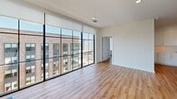 Located at 2922 W Marshall St in Richmond, VA, this 3-bedroom, single-floor unit offers a thoughtfully designed open-concept layout with modern finishes throughout. The combined kitchen and living area serves as the heart of the home, featuring warm hardwood-style flooring that extends seamlessly across the entire unit. The kitchen is appointed with sleek white cabinetry, contrasting dark wood accent cabinets, a striking quartz waterfall island with an undermount sink, stainless steel appliances including a range, built-in microwave, and refrigerator, and a clean subway tile backsplash. Recessed lighting adds a polished touch to the space. The living area is a true standout, boasting dramatic floor-to-ceiling windows with bold black framing that flood the space with natural light and offer expansive views of the surrounding Richmond cityscape. Each of the three bedrooms is well-proportioned, with ceiling fans, large windows, and neutral walls that create a bright and airy atmosphere. The generously sized primary bedroom includes access to two closets, both fitted with wire shelving systems for organized storage. The clean, contemporary aesthetic, abundant natural light, and urban views make this a highly functional and visually appealing residence.