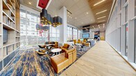 Located at 1717 N 12th St in Philadelphia's vibrant North Philadelphia neighborhood, this single-floor amenity lounge — known as Vantage — spans an impressively generous footprint designed to foster community, comfort, and productivity. The space is defined by its soaring double-height ceilings and expansive floor-to-ceiling glass curtain walls that flood the interior with abundant natural light and offer sweeping views of the surrounding urban landscape, including distant glimpses of the Philadelphia skyline.

The interior design balances modern sophistication with welcoming warmth. Rich hardwood flooring anchors the open-plan layout, complemented by bold, abstract blue-and-gold patterned area rugs that delineate distinct lounge zones. Plush leather seating in cognac and mustard tones is arranged in flexible groupings, ideal for both social gatherings and quiet relaxation. Dramatic cloud-form pendant light fixtures with gold interiors serve as artistic focal points throughout.

A central feature wall showcases the Vantage branding alongside a sleek double-sided fireplace and a large-screen television. Built-in bookcase displays add a curated, residential touch. A games area with a foosball table, collaborative work tables with bar seating, and a dedicated study bar round out the multi-functional offerings, making this an all-encompassing social and wellness hub.