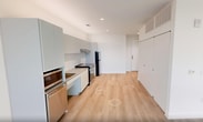 This contemporary 650 square foot apartment, located at 620 Foster Street in Durham, NC, offers a blend of modern design and functionality. The single-floor layout comprises an open-concept kitchen and living area, a hallway, and a bathroom. The space is characterized by its abundant natural light, courtesy of large windows that provide stunning city views.

The kitchen is a highlight, featuring sleek white cabinetry, stainless steel appliances, and a subway tile backsplash. It's equipped with a range, microwave, and refrigerator, making it ideal for cooking and entertaining. The living area flows seamlessly from the kitchen, offering a versatile space for relaxation and dining.

The bathroom is designed with accessibility in mind, featuring a walk-in shower with grab bars, a handheld showerhead, and ample space for mobility. The green flooring adds a subtle pop of color to the otherwise neutral palette.

Throughout the apartment, light wood-look flooring creates a warm and inviting atmosphere, while the white walls enhance the sense of spaciousness. The large windows not only flood the rooms with natural light but also offer panoramic views of the Durham skyline, connecting the interior space with the urban environment outside.

This apartment combines modern aesthetics with practical living, making it an ideal urban dwelling for those seeking a contemporary lifestyle in the heart of Durham.