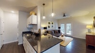 Located at 1649 SR-12 N in Ashland City, Tennessee, this single-story residence offers a thoughtfully designed layout with modern finishes and a cohesive aesthetic throughout. The open-concept kitchen flows seamlessly into the living area, anchored by a granite-topped island with an undermount sink and pendant lighting. White shaker cabinetry pairs elegantly with dark granite countertops, while stainless steel appliances complete the well-equipped kitchen. Rich hardwood flooring runs through the main living areas, adding warmth and continuity. The living room is bright and welcoming, featuring a ceiling fan, french doors that invite natural light, and outdoor views. A dedicated dining area with a pendant light and natural window light offers an ideal space for meals and gatherings. The bedrooms are carpeted and comfortable, each benefiting from ample natural light through large windows. A spacious walk-in closet with dual wire shelving provides generous storage. The bathroom is finished with clean white subway tile in the tub surround and dark granite vanity countertops, delivering a crisp, contemporary feel. The overall ambiance is modern yet inviting, with consistent design choices that create a harmonious living environment.