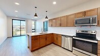 Located in the vibrant East Nashville neighborhood, this single-floor unit at 715 S Seventh St offers a thoughtfully designed layout with modern finishes throughout. The open-concept kitchen serves as the heart of the space, featuring warm-toned shaker-style cabinetry, white quartz countertops, a classic subway tile backsplash, and a full suite of stainless steel appliances including a refrigerator, electric range, over-the-range microwave, and dishwasher. Stylish pendant lighting hangs above the peninsula sink, adding an inviting ambiance. Light wood-tone flooring flows consistently throughout the living areas and bedrooms, contributing to a clean, cohesive aesthetic. Multiple bedrooms offer ceiling fans, natural light through large windows with blinds, and generous proportions. Several rooms provide direct access to a private balcony through sliding glass doors framed in matte black, offering pleasant outdoor views of surrounding greenery. The bathrooms are finished with large-format tile flooring, warm wood vanities, white countertops, and contemporary globe sconce lighting. A spacious walk-in closet with wire shelving provides ample storage. The unit's neutral palette and modern detailing create a bright, functional living environment.