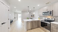 This single-floor residence showcases a thoughtfully designed open-concept layout with a clean, modern aesthetic. Light wood-tone flooring flows throughout the main living areas, enhancing the bright, airy atmosphere created by recessed lighting and crisp white walls.

The kitchen serves as the heart of the space, featuring two-tone cabinetry — light upper cabinets paired with wood-grain lower units — complemented by a white quartz peninsula with an undermount sink. Stainless steel appliances, including a range, microwave, and dishwasher, add a polished touch, while a geometric hexagonal tile backsplash introduces subtle texture. Pendant lights hang above the peninsula, which doubles as a casual dining and seating area with bar stools. The kitchen opens seamlessly into the living and dining areas, creating an ideal flow for everyday living.

The bedroom offers a calm, neutral retreat with warm accent tones introduced through furnishings and artwork. The space is comfortably scaled with ample room for a full bedroom suite.

The bathroom is finished with dark polished floor tiles, a wood-tone vanity with a marble-style countertop, a round mirror, and a full subway-tiled tub surround, combining timeless and contemporary elements throughout.