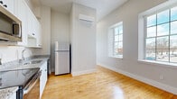 Located at 56 St Joseph St in Fall River, MA, this 2-bedroom, 1-bathroom unit offers a thoughtfully designed layout across a single floor. Warm hardwood flooring runs throughout the space, lending a cohesive and inviting feel to every room.

The kitchen is well-appointed with white shaker-style cabinetry, granite countertops, and a full suite of stainless steel appliances including a range, microwave, dishwasher, and refrigerator. A wall-mounted mini-split unit provides efficient climate control for the open kitchen and living area. Tall ceilings add to the sense of openness, and a window brings in natural light from the street.

The bedrooms are bright and functional, with large double-hung windows framing neighborhood views. The primary bedroom offers generous space and includes a built-in closet with bi-fold doors. The second bedroom is similarly finished with the same hardwood flooring and clean neutral walls.

The bathroom is neatly appointed with a white vanity, a framed mirror, tile flooring in a basketweave pattern, and a full tub-shower combination enclosed by sliding glass doors.

Overall, the unit presents a clean, modern aesthetic with practical finishes, making it a functional and comfortable residence in the Fall River community.