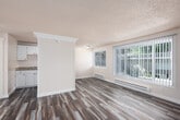 This single-floor space offers a clean, practical layout with a consistent design language throughout. The living area is a standout feature, boasting large windows dressed with vertical blinds that allow generous natural light to fill the room. Durable wood-look vinyl plank flooring runs throughout the entire space, adding warmth and continuity. A textured ceiling and baseboard heating units are present in multiple rooms, providing both character and comfort.

A distinctive beadboard partition wall serves as an architectural divider, adding visual interest and structure to the open living and dining area. The kitchen is efficiently designed with crisp white cabinetry, granite-style countertops, a stainless steel sink, and an electric range, offering practical functionality in a compact footprint.

A secondary room features its own window with blinds and a baseboard heater, making it a versatile space suitable as a bedroom or home office. The bathroom is bright and well-finished, featuring a white vanity with a granite-style countertop, a large mirror with overhead lighting, and a combined tub and shower. Throughout the space, the neutral color palette and clean finishes create a cohesive, move-in-ready atmosphere.