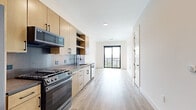 Located in Denver's vibrant Cole neighborhood, this one-bedroom, one-bathroom unit at 1300 40th St offers a thoughtfully designed modern living space across a single floor. Light hardwood flooring flows throughout, complementing the clean white walls and creating a bright, cohesive aesthetic.

The open kitchen is a standout feature, outfitted with warm light wood cabinetry, dark hardware, a full-height tile backsplash, dark countertops, and stainless steel appliances including a gas range, built-in microwave, refrigerator, and dishwasher. Open shelving adds both function and style to the kitchen design.

The living area extends toward a large sliding glass door with a balcony, allowing ample natural light and offering views of the Denver skyline — a striking backdrop visible from both the living space and the generously sized bedroom. The bedroom features its own large black-framed window that frames panoramic city views, with warm hardwood flooring continuing throughout.

The bathroom is finished with large-format tile flooring, a wood vanity with a white countertop, and in-unit washer and dryer access conveniently located in the adjacent closet. The walk-in closet provides built-in shelving and hanging rods for practical storage. This unit combines modern finishes with functional design in a prime Denver location.