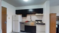 Located at 364 W Lane Ave in Columbus, Ohio, this single-floor studio unit offers a functional and efficient layout designed to maximize every square foot. The main living area serves as both a sleeping and lounge space, featuring tile flooring, a textured ceiling, and a window that brings in natural light and exterior views. A wall-mounted unit provides climate control, and a large decorative mirror adds depth to the room.

The kitchen is situated along one wall and is well-equipped for everyday cooking. It features bold dark cabinetry contrasted against light tile backsplash walls, a stainless steel apron-front sink with a modern pull-down faucet, granite-style countertops, a stainless steel dishwasher, an electric coil range, and a full-size refrigerator. A range hood is mounted above the stove, and ample upper cabinet storage is provided.

The bathroom is clean and compact, appointed with a wood-toned vanity, a stone-pattern countertop, a wall-mounted medicine cabinet with mirror, a toilet, and a full shower-tub combination with a curtain. Tile flooring completes the space. Overall, the unit provides a practical and self-contained living environment well-suited for individuals seeking a straightforward, no-frills residence in Columbus.