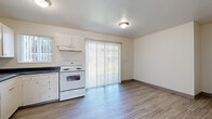 Located at 535 C St in Washougal, Washington, this two-story home offers a well-organized layout divided evenly across two floors. The main level hosts the kitchen and living areas, while the upper floor accommodates the bedrooms and additional bathroom, connected by carpeted staircases. The kitchen is equipped with white cabinetry, dark countertops, and white appliances including a range, dishwasher, and refrigerator. Wood-look vinyl flooring runs throughout the kitchen and lower-level areas, lending a clean and cohesive feel. A sliding glass door with vertical blinds in the kitchen area allows natural light to filter in and provides outdoor access. The living room features carpeting and a large window with vertical blinds, allowing for ample natural light and a bright, airy atmosphere. A baseboard heating system is present for climate control. Both bedrooms are carpeted and offer a neutral palette with clean white walls. The primary bedroom is generously sized and includes an open closet with a full-length hanging rod and shelf. The bathrooms are functional and straightforward, with one featuring a full tub-shower combination and wood-look vinyl flooring. Overall, the home presents a clean, practical, and move-in-ready living environment.