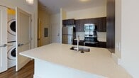 Located at 180 Eastern Ave in Malden, Massachusetts, this well-appointed single-floor residence offers a thoughtfully designed open-concept layout that seamlessly connects the living, dining, and kitchen areas. Rich hardwood flooring spans the main living spaces, complemented by warm neutral walls and track lighting that enhances the bright, airy ambiance. Large windows invite abundant natural light throughout.

The kitchen is a standout feature, showcasing a generous quartz-topped island with an undermount sink, dark espresso cabinetry, and a full suite of stainless steel appliances including a refrigerator, range, and microwave. The layout provides excellent flow for both everyday living and entertaining.

A dedicated laundry area with stacked washer and dryer units offers added convenience within the unit. The carpeted bedroom provides a comfortable retreat, with windows overlooking lush greenery that bring a sense of calm and connection to the outdoors.

The bathroom is clean and modern, featuring large-format tile flooring, a walk-in shower with white tile surround, and dark wood cabinetry for storage. A hallway connects the bedroom to the main living area, offering easy access to the bathroom and closet space. Overall, this residence presents a polished, contemporary living environment with functional design and quality finishes throughout.
