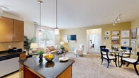 This thoughtfully designed 2-bedroom, 2-bathroom residence in Cherry Hill, New Jersey offers a functional and stylish single-floor layout. The open-concept living, dining, and kitchen area forms the heart of the home, bathed in natural light from large windows dressed with blinds and sheer curtains. The kitchen is a standout feature, boasting warm wood cabinetry, dark granite countertops, stainless steel appliances, track lighting, and a central island with bar seating — perfect for casual dining or entertaining. Adjacent to the kitchen, the dining area comfortably accommodates a round table and features vaulted-style ceilings with track lighting. The living room is inviting and bright, with plush carpeting and views of the outdoors. The primary bedroom is generously sized, complete with soft carpet, a walk-in closet, and access to a private en suite bathroom featuring a glass-enclosed shower and warm tile finishes. The second bedroom is equally comfortable, with natural light streaming through a large window. A second full bathroom offers a tiled soaking tub and shower combination. Throughout the residence, warm neutral tones and consistent finishes create a cohesive, welcoming ambiance.