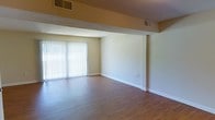 This two-floor space offers a clean, functional layout designed to maximize comfort and usability across both levels. The main living area is immediately welcoming, featuring warm hardwood flooring that runs throughout and lends a sense of continuity and warmth to the space. Neutral, light-toned walls provide a versatile backdrop, making the area adaptable to a variety of interior styles and furnishing choices. A large sliding glass door, dressed with vertical blinds, serves as a prominent architectural feature, allowing an abundance of natural light to fill the room while providing convenient access to the outdoors. Structural ceiling beams add a subtle architectural detail overhead, complementing the textured ceiling finish. Dual HVAC vents are positioned thoughtfully to ensure consistent climate control throughout. Clean white baseboards frame the perimeter of the room, adding a crisp, finished look to the overall aesthetic. The open, unobstructed layout of the main living area creates a spacious feel, offering flexibility in how the space can be arranged and utilized. With its practical design elements and bright, airy atmosphere, this two-floor space presents a solid foundation for comfortable everyday living.