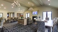 Located at 5315 Avery Road in Dublin, Ohio, this single-floor community space offers a refined and welcoming atmosphere designed for comfort and socializing. The open-concept layout seamlessly connects the lounge and dining areas, creating a generous, flowing interior ideal for gatherings of all sizes.

The space is anchored by soaring vaulted ceilings with exposed beam detailing, which lend an airy, grand quality to the room. Two elegant multi-arm crystal chandeliers serve as focal points overhead, casting warm, ambient light throughout. Recessed lighting complements the chandeliers, ensuring the space is well-lit at all hours.

A classic white fireplace with a traditional mantle adds a cozy centerpiece to the lounge area, above which a wall-mounted television is positioned for easy viewing. Comfortable upholstered seating is arranged thoughtfully around the fireplace, encouraging relaxed conversation. A built-in display cabinet and a media console in a light wood finish add both function and style to the room.

The dining area features formal seating with patterned chairs, suitable for communal meals or events. A bold, nature-inspired patterned carpet in dark tones ties the space together, adding visual depth and sophistication. French-style windows and glass panel doors allow natural light to filter in while offering views to the outdoors, enhancing the overall sense of openness.