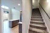 This well-designed two-story home offers a thoughtful layout across two levels, combining modern aesthetics with functional living spaces. The main floor features a generous open-concept kitchen and living area bathed in natural light, with soaring ceilings that lend an impressive sense of volume. The kitchen is outfitted with rich dark wood cabinetry, stainless steel appliances including a refrigerator, range, microwave, and dishwasher, complemented by crisp white countertops and a central island with additional storage. Light hardwood flooring flows throughout the main level, enhancing the bright, airy atmosphere. A sliding glass door opens directly to a private balcony, offering outdoor views of the surrounding neighborhood. An in-unit stacked washer and dryer adds everyday convenience. Carpeted stairs lead to the upper level, where the bedroom provides a comfortable retreat complete with plush carpet, a ceiling fan, and dual windows overlooking the exterior. Two closets offer ample storage, and the full bathroom features light hardwood flooring and a clean, neutral palette. A hallway connects the upper-level rooms seamlessly. The overall design is clean, contemporary, and move-in ready.