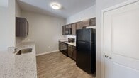 This single-story residence in San Marcos, Texas, offers a practical and modern layout across three bedrooms and two full bathrooms. The interior is finished with wood-look luxury vinyl plank flooring throughout the main living and bedroom areas, complemented by light tile in the bathrooms, creating a cohesive and easy-to-maintain aesthetic.

The kitchen serves as a functional centerpiece, featuring dark espresso cabinetry, light granite-style countertops, a kitchen island with undermount sink, and black appliances including a refrigerator, range, and built-in microwave. The kitchen flows openly into the living and dining areas, enhancing the sense of space and connectivity.

The bedrooms are generously sized, each equipped with closets offering built-in rod storage. Ceiling fans are present in select bedrooms, and windows allow natural light and exterior views. The bathrooms mirror the kitchen's design language, with matching dark cabinetry, granite-style countertops, and a tub-shower combination.

A hallway connects the entry to the private areas of the home, with additional storage closets visible along the corridor. The overall palette of soft grays and whites creates a clean, neutral ambiance throughout.