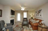 This single-story residence offers a thoughtfully designed layout that accommodates comfortable everyday living across several distinct spaces. The living room serves as the heart of the home, featuring a ceiling fan with light fixture, a fireplace, and a front entry door flanked by windows that allow natural light to filter in. Warm-toned carpet, a decorative area rug, and a large world map wall canvas contribute to the room's inviting character.

Adjacent to the living area, the dining space features pendant lighting above a wooden dining table with seating for several guests, complemented by decorative wall art. The kitchen is efficiently arranged with warm wood cabinetry, gray laminate countertops, a full suite of white appliances including a range with overhead microwave, and a dishwasher.

The primary bedroom is carpeted and includes a ceiling fan, natural light from a window, dark wood furnishings, and direct access to a private en-suite bathroom. This bathroom features tile flooring, a vanity with warm wood cabinetry, and a tub-shower combination. A second well-sized bedroom also features carpet flooring, a ceiling fan, and a window. The second full bathroom mirrors the first in layout, offering tile flooring, a wood-tone vanity, and a tub-shower combination.