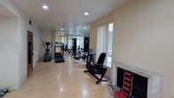This dedicated fitness facility is designed to support a comprehensive workout experience within a clean, functional environment. The space features light hardwood flooring that runs the length of the room, contributing to a bright and open atmosphere. Recessed ceiling lighting provides consistent illumination throughout, while large windows along one wall allow natural light to fill the area, creating an inviting workout environment.

A full-length mirrored wall on one side visually expands the space and allows users to monitor their form during exercise. The facility is equipped with a variety of cardio machines, including a treadmill, an elliptical trainer, and a recumbent stationary bike, making it suitable for a range of cardiovascular workouts. A multi-station cable machine and a weight bench are also present, offering strength training options for a well-rounded fitness routine.

The neutral, light-toned walls and uncluttered layout contribute to a calm and focused atmosphere. A door provides access to an adjoining area, adding convenience to the overall layout. The space is thoughtfully arranged to maximize usability while maintaining clear pathways between equipment, ensuring a safe and efficient environment for exercise.