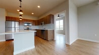 Located at 5567 Odana Rd in Madison, Wisconsin, this modern single-floor unit offers a thoughtfully designed open-concept layout that seamlessly connects the kitchen, dining, and living areas. Light wood-tone flooring flows throughout, creating a warm and cohesive aesthetic.

The kitchen is a standout feature, showcasing rich walnut-toned cabinetry, a geometric hexagonal tile backsplash, and sleek white quartz countertops. A full suite of stainless steel appliances — including a range, built-in microwave, dishwasher, and refrigerator — provides a well-equipped cooking space. A central island with pendant lighting above adds both prep space and a casual gathering spot.

The expansive living area benefits from large windows and a sliding glass door that invite abundant natural light and offer views of the surrounding landscape. A ceiling fan enhances comfort in this generously sized room.

The bathrooms are finished with the same walnut-toned cabinetry, white quartz countertops, and wood-look flooring, maintaining a consistent modern style throughout. Each bathroom includes a tub/shower combination, a large mirror, and built-in niche shelving for storage.

Overall, the unit presents a clean, contemporary design with quality finishes and a bright, open ambiance well-suited to modern living in Madison, WI.