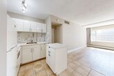 Located at 10020 103 Avenue NW in the heart of downtown Edmonton, Alberta, this single-floor studio unit offers a thoughtfully organized open-concept layout that maximizes every square foot of available space. The kitchen is positioned at the entry end of the unit and features white cabinetry, a striking marble-style tile backsplash, white appliances including a refrigerator and stove, and a peninsula island that provides additional counter space and helps define the kitchen zone. Large-format beige ceramic tiles cover the kitchen and entryway floors, lending a clean and cohesive look to the area. A convenient entry closet with open shelving offers practical storage directly at the front door. The living area extends from the kitchen, finished with light-toned hardwood flooring that adds warmth and visual continuity throughout the space. A wide window with draping curtains allows natural light to fill the room and provides views of the surrounding urban landscape. The textured ceiling adds a subtle architectural detail consistent throughout the unit. The full bathroom is finished with beige ceramic floor and wall tiles, a white vanity with an integrated sink, and a bathtub-shower combination. The overall palette of warm neutrals and white creates a bright, clean, and functional living environment well-suited to urban living in Edmonton's vibrant downtown core.