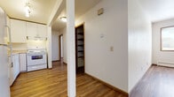 Located at 1001 Gilbert Rd in Madison, Wisconsin, this single-floor unit offers a clean, functional layout with consistent wood-look flooring running throughout every room, creating a warm and cohesive aesthetic. The kitchen is well-appointed with white cabinetry offering ample upper and lower storage, a stainless steel sink, laminate countertops, a white electric range, and a full-size refrigerator. A range hood provides ventilation, and the open sightlines connect the kitchen naturally to the adjacent hallway and living areas. The hallway features a structural column detail and an open built-in shelving unit, providing convenient storage and organizational space. The living area is open and airy, with white walls, warm-toned wood-look flooring, and a window that admits natural light, adding brightness to the space. A baseboard heating system runs along the walls, ensuring comfortable temperatures throughout the year. The bedroom is a calm, well-proportioned room with its own window fitted with blinds for privacy and natural light control, along with baseboard heating. The bathroom is finished with white square tile surrounding the full-size soaking tub and shower combination, complemented by a white vanity with raised-panel cabinetry and stone-look tile flooring, offering a clean and timeless look.