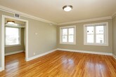 This single-floor residence offers a thoughtfully arranged layout with a cohesive, neutral color palette and an abundance of natural light streaming through multiple windows fitted with blinds. The living areas are anchored by warm, honey-toned hardwood flooring that extends throughout, complemented by clean white crown molding and baseboards that lend a classic, polished character to the space. The main living room is generously sized, featuring a ceiling fan with integrated lighting and dual windows that frame views of the surrounding neighborhood, creating a bright and airy atmosphere. A ceiling fan in one of the additional rooms provides both comfort and a finishing touch. The kitchen is efficiently designed with light wood cabinetry offering ample storage, dark countertops, and stainless steel appliances including a refrigerator, range, and over-the-range microwave. Light tile flooring and a built-in counter extension add practicality to the space. The bathroom is finished in classic white subway tile, featuring a wall-mounted porcelain sink with chrome fixtures, a full soaking tub with shower, a medicine cabinet mirror, and a window for natural ventilation. Throughout the residence, the consistent use of soft gray wall tones, white trim, and natural materials creates a harmonious and inviting environment.