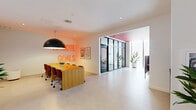 Located in Miami, FL, this single-floor business center delivers a compact yet thoughtfully designed workspace that balances creativity with functionality. The interior is defined by a bold color palette — vivid red and pink painted ceilings contrast against crisp white walls and light polished concrete flooring, creating an energetic yet professional atmosphere throughout.

The space features a glass-partitioned game room enclosed by sleek black-framed floor-to-ceiling glass walls, offering visual openness while maintaining acoustic separation. Inside, a bright yellow communal table is surrounded by deep red ergonomic chairs beneath suspended linear pendant lighting. A glowing neon "Remote Goals" sign adds a motivational, modern touch to the collaborative area.

The open workspace beyond the partitions includes a large wooden conference table with cushioned seating, accompanied by curated wall art and a statement black dome pendant light. A sideboard with sculptural décor and framed artwork adds warmth and character to the breakout area nearby.

A corridor lined with tall glass partitions, lush potted plants, and soft drapery leads to private workstations fitted with navy acoustic privacy panels — ideal for focused, heads-down work. Recessed lighting throughout ensures consistent, comfortable illumination across all zones, making this business center a well-rounded environment for both collaboration and individual productivity.