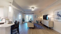 Located at 3650 RCA Blvd in Palm Beach Gardens, Florida, this single-story residence showcases a cohesive coastal aesthetic carried throughout each room. The open-concept living area serves as the heart of the home, featuring warm wood-look flooring, tray ceilings with crown molding, and a ceiling fan. Large French doors flood the space with natural light and lead to a private balcony, while nautical-themed artwork reinforces the relaxed Florida atmosphere. A glass-top coffee table and comfortable neutral seating complement the bright, airy palette.

The kitchen is outfitted with white cabinetry, quartz countertops, stainless steel appliances including a range with a stainless hood, and a subtle tile backsplash. An adjacent dining area accommodates a round table with upholstered chairs beneath a bold wave-inspired canvas.

The bedrooms offer a serene retreat, each featuring tray ceilings, plush carpeting, and windows with ample natural light. The primary bedroom includes generous closet space and a well-appointed en-suite bathroom with a glass-enclosed walk-in shower, tile flooring, and a vanity with ample storage. The overall ambiance is calm, polished, and distinctly coastal.