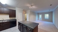 Located at 2000 Teaching Dr in Cary, NC, this single-floor residence offers a well-designed, open layout that connects the kitchen and living areas seamlessly. The kitchen is a standout feature, showcasing rich dark wood cabinetry, granite-style countertops, and a central island that provides additional prep and storage space. Black appliances — including a refrigerator, range, and dishwasher — complement the cabinetry, while light tile flooring ties the space together. Crown molding throughout the main living areas adds a refined architectural detail, and neutral-toned walls create a clean, versatile backdrop. The living area features plush carpeting, crown molding, and a window that draws in natural light. Bedrooms are generously sized with soft carpet flooring, ceiling fans, and windows offering views of the surrounding greenery. Closet space is well-appointed, with at least one bedroom featuring a walk-in closet with built-in shelving. The bathrooms are finished with tile flooring, and include a shower/tub combination with chrome fixtures. Overall, the space presents a functional and comfortable layout suited for everyday living in a convenient Cary location.