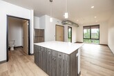 This thoughtfully designed 1-bedroom, 1-bathroom unit offers a contemporary living experience across a single floor. The open-concept kitchen and living area serves as the heart of the unit, showcasing a central island with a sleek white quartz countertop and warm wood-toned cabinetry fitted with brushed nickel hardware. Stainless steel appliances — including a range, microwave, dishwasher, and refrigerator — complete the kitchen, while pendant lighting adds a modern touch overhead. Light hardwood flooring runs throughout the entire unit, creating a cohesive and bright atmosphere.

The living area benefits from large, black-framed windows that flood the space with natural light and offer views of the surrounding urban landscape and greenery. The bedroom is a calm, well-proportioned retreat, also featuring oversized windows that frame treetop and cityscape views, with recessed lighting above.

The bathroom is clean and functional, equipped with a glass-enclosed walk-in shower with brushed nickel fixtures. A dedicated laundry area includes a stacked washer and dryer unit, adding everyday convenience. Throughout the space, the design emphasizes clean lines, neutral tones, and quality finishes, creating a modern and comfortable urban living environment.
