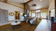 Located at 21200 East Country Vista Drive in Spokane, WA, this single-story community clubhouse offers a thoughtfully designed gathering space with a warm, lodge-inspired aesthetic. The centerpiece of the facility is a dramatic great room boasting soaring vaulted ceilings with exposed wood beam accents and a floor-to-ceiling stacked stone fireplace that anchors the space with rustic elegance. A statement windmill-style pendant fan adds a distinctive architectural touch overhead. Large French doors and expansive windows flood the room with natural light and provide views of the surrounding outdoors. Comfortable seating arrangements with neutral-toned chairs and accent tables invite conversation and relaxation throughout the open layout.

The clubhouse also features a dedicated fitness center equipped with cardio machines, a multi-station strength training unit, exercise balls, and medicine ball racks — all set within a well-lit, carpeted space with natural window light. A separate lounge area with plush leather seating and a wall-mounted display offers a cozy media retreat. A game room with a billiards table and built-in cabinetry with ample countertop space rounds out the amenities. The entry foyer features tile flooring, a wood-paneled ceiling with warm Edison-style lighting, and generous glazing that creates a bright and welcoming arrival experience throughout.