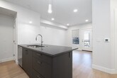 This well-designed one-bedroom, one-bathroom residence in Meridian, Idaho offers a clean, modern aesthetic with thoughtful finishes throughout. The open-concept living and kitchen area creates an efficient, connected layout anchored by a large central island with a sleek gray countertop, an undermount sink, and pendant lighting overhead. The kitchen is outfitted with white cabinetry extending to the ceiling, dark countertops, a subway tile backsplash, and a full suite of stainless steel appliances including a french door refrigerator, range, and over-the-range microwave. Light hardwood flooring runs continuously throughout the space, complementing the crisp white walls and recessed lighting that keep the interior bright and airy. The bedroom is a comfortable size, featuring two windows that allow natural light to fill the room, with window shades providing privacy and light control. Three closets offer generous storage options throughout the unit. The bathroom is finished with a white vanity, dark countertop, a backlit mirror, and a full tub-shower combination. The overall ambiance is clean, contemporary, and functional — well suited for modern living.