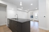 This well-designed one-bedroom, one-bathroom residence in Meridian, Idaho offers a clean, modern aesthetic with thoughtful finishes throughout. The open-concept living and kitchen area creates an efficient, connected layout anchored by a large central island with a sleek gray countertop, an undermount sink, and pendant lighting overhead. The kitchen is outfitted with white cabinetry extending to the ceiling, dark countertops, a subway tile backsplash, and a full suite of stainless steel appliances including a french door refrigerator, range, and over-the-range microwave. Light hardwood flooring runs continuously throughout the space, complementing the crisp white walls and recessed lighting that keep the interior bright and airy. The bedroom is a comfortable size, featuring two windows that allow natural light to fill the room, with window shades providing privacy and light control. Three closets offer generous storage options throughout the unit. The bathroom is finished with a white vanity, dark countertop, a backlit mirror, and a full tub-shower combination. The overall ambiance is clean, contemporary, and functional — well suited for modern living.