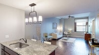 Located at 526 E Superior Ave in Cleveland, OH, this well-appointed one-bedroom, one-bathroom residence offers a thoughtfully designed single-floor layout. Rich hardwood flooring flows throughout the main living areas, anchoring a bright, open-concept space that seamlessly integrates the living room, dining area, and kitchen.

The kitchen is a standout feature, equipped with stainless steel appliances including a refrigerator, range, and microwave. White shaker-style cabinetry pairs with granite countertops and a tile backsplash, while a peninsula with a built-in sink and additional seating adds both function and style. A multi-pendant chandelier defines the dining zone adjacent to the kitchen.

The living room is spacious and airy, illuminated by a ceiling fan and accented with soft blue walls, creating a calm and inviting atmosphere. The bedroom features plush carpeting, a ceiling fan, a large window with outdoor views, and a recessed nook ideal for bed placement. An impressively generous six closets throughout the unit provide exceptional storage capacity, including a walk-in closet with wire shelving.

The bathroom is finished with tile flooring, a granite-topped white vanity, a framed mirror, and a full soaking tub with subway tile surround. A long hallway with recessed lighting connects the rooms with clean, neutral tones throughout.