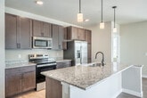 Located at 856 N Main St in Oregon, Wisconsin, this well-appointed single-floor home offers a thoughtfully designed layout with 2 bedrooms and 2 bathrooms. The open-concept kitchen and living area serves as the heart of the home, featuring rich dark wood cabinetry, a large granite-topped island with a undermount sink, stainless steel appliances including a refrigerator, range, and microwave, and elegant pendant lighting overhead. Light hardwood flooring flows throughout the main living spaces, complemented by neutral tones and abundant natural light streaming through multiple windows and a sliding glass door that opens to the outdoors. The spacious living area includes a ceiling fan and offers a bright, airy atmosphere. Both bedrooms are carpeted for comfort, with the primary bedroom offering a generous walk-in closet outfitted with built-in shelving and hanging rods. The two bathrooms are finished with granite-topped dark wood vanities and oil-rubbed bronze fixtures. The primary bath features a double-sink vanity with a large mirror and a walk-in shower, while the second bathroom includes a soaking tub/shower combination. Clean lines, modern hardware, and consistent finishes throughout give this home a cohesive and contemporary feel.