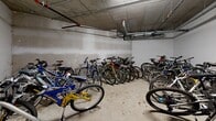 Located at 733 Goldstream Ave in Langford, BC, this dedicated indoor bicycle storage room provides a secure and functional space for residents to store their bikes year-round. The room features a concrete construction throughout, with exposed concrete ceilings and painted concrete block walls that reflect its utilitarian, durable design. Overhead, a network of pipes and conduits runs along the ceiling, supplying building utilities while leaving the floor space fully accessible. The room is equipped with multiple metal bicycle racks anchored to the floor, providing organized storage for a large number of bikes of varying styles, including mountain bikes and road bikes. A wall-mounted utility shelf and additional equipment are present near the entrance, offering a convenient space for bike maintenance tools and accessories. The concrete floor provides a sturdy, easy-to-clean surface well-suited for the heavy use this space sees. Access to the room is provided via a solid door, ensuring security for stored bicycles. Overall, this space is a practical and well-appointed amenity that caters to cycling enthusiasts and everyday commuters alike, reflecting the active lifestyle of the Langford community.