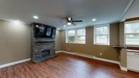 This single-floor space is thoughtfully designed with consistent warm, earthy tones and rich wood-look flooring that flows throughout every room, creating a cohesive and inviting atmosphere.

The living area serves as a focal point, anchored by a striking stacked-stone fireplace wall with a built-in shelf and wall-mounted television above. Multiple windows allow natural light to fill the room, while recessed lighting and a ceiling fan provide additional comfort. A baseboard heating system runs along the exterior walls.

The kitchen is well-appointed with white shaker-style cabinetry featuring black hardware, rich butcher block countertops, and stainless steel appliances including a gas range, microwave, and refrigerator. A peninsula with seating provides casual dining space, and pendant lighting adds character. Windows overlooking the outdoors brighten the area naturally.

The bathroom features a white vanity with a dark oil-rubbed bronze faucet and fixtures, a framed mirror with industrial-style lighting, and a tiled walk-in shower enclosed with glass doors.

A bedroom includes a ceiling fan, a window with natural light, baseboard heating, and access to a walk-in closet, completing this well-finished and functional single-level space.