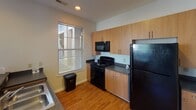 Located along Abbey Court Drive in Charlotte, NC, this single-story unit offers a thoughtfully arranged floor plan with clearly defined living, sleeping, and functional spaces. The living area is generously sized, featuring wall-to-wall carpeting, a ceiling fan, and multiple windows fitted with horizontal blinds that allow ample natural light to filter throughout. The open feel of the space is reinforced by neutral-toned walls and clean white trim.

The kitchen is accessible directly from the living area and features a peninsula-style counter that creates a natural divide between the two spaces. Light wood cabinetry provides substantial storage, complemented by dark granite-style countertops and a full suite of black appliances, including a range, built-in microwave, and refrigerator. Wood-look flooring runs through the kitchen, adding warmth and practicality.

The bedroom offers a quiet, carpeted retreat with a well-sized window that brings in natural light. The bathroom includes a dual-sink vanity with dark countertops, white cabinetry below, a large mirror with overhead vanity lighting, and a walk-in shower. A closet is accessible from the bathroom area, adding convenient storage. Overall, the unit presents a functional and comfortable living environment.
