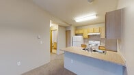 Located in Spokane Valley, WA, this one-bedroom, one-bathroom unit offers a functional and well-organized single-floor layout. The open-concept kitchen is equipped with light wood cabinetry, ample upper and lower storage, a white appliance suite including a refrigerator and electric range, and a peninsula countertop that extends into the living area, creating a natural divide between cooking and living spaces. The light-toned countertops and tile flooring add a clean, practical finish to the kitchen. Conveniently tucked just off the kitchen is an in-unit laundry area with a full-size washer and dryer and an overhead shelf for additional storage. The carpeted living room is bright and open, featuring a sliding glass door that leads to a private balcony with outdoor views. The bedroom is a comfortable size, featuring carpet flooring, a window that brings in natural light, and a dedicated closet for storage. The full bathroom features light wood cabinetry, a wide vanity with ample counter space, a large mirror, and tile flooring. Neutral tones and textured ceilings are consistent throughout, giving the unit a cohesive and move-in-ready feel. A hallway connects the main living areas smoothly, enhancing the overall flow of the space.