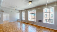 Located on Willow Street in Mount Airy, North Carolina, this single-floor unit showcases a thoughtful blend of industrial heritage and contemporary upgrades. The open living areas are defined by warm, polished hardwood floors that run throughout, reflecting natural light from a series of large, multi-pane factory-style windows. Beadboard ceilings with exposed utility conduits and ceiling fans reinforce the building's industrial roots while maintaining a clean, airy atmosphere.

The kitchen is well-appointed with dark espresso cabinetry, granite countertops, a spacious island with a double undermount sink, stainless steel appliances, and industrial-style pendant lighting overhead. Additional windows in the kitchen bring in generous natural light and views of the surrounding brick exteriors.

The bedrooms feature the same hardwood flooring, ceiling fans, and bright windows. One bedroom showcases a striking exposed brick accent wall, adding raw architectural texture to the space. A bold red barn-style sliding door serves as a distinctive design element in one of the living areas.

The bathrooms are finished with clean white tub-shower combinations, hardwood flooring, and granite-topped vanities with dark wood cabinetry, maintaining a consistent material palette throughout the unit.