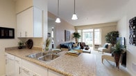 This single-floor residence offers a thoughtfully designed layout that balances comfort and functionality. The open-concept living and dining area is bright and welcoming, anchored by large sliding glass doors that flood the space with natural light and provide views of the surrounding greenery. Soft neutral tones on the walls complement the plush carpeting underfoot, creating a warm and cohesive ambiance throughout.

The galley-style kitchen is efficiently organized with white cabinetry, granite-style countertops, and a full suite of white appliances, including a refrigerator, electric range, and built-in microwave. Pendant lighting above the adjoining breakfast bar adds a stylish touch, while wood-look flooring grounds the space with a clean, modern feel.

The residence includes multiple bedrooms, each featuring plush carpet, generous natural light from well-placed windows, and ample closet space with built-in shelving. Ceiling fans in select bedrooms enhance comfort year-round.

The bathroom is well-proportioned, featuring a granite-style vanity with white cabinetry, wood-look flooring, and a shower-tub combination. Neutral wall tones tie seamlessly into the overall design palette of the home, delivering a consistent and inviting atmosphere from room to room.
