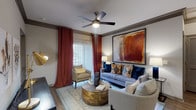 This well-appointed single-floor residence showcases a cohesive design aesthetic that combines modern finishes with warm, inviting tones throughout. The living area serves as the heart of the home, featuring crown molding, a ceiling fan, and a large window dressed with dramatic floor-to-ceiling drapes that allow natural light to filter in. The open-concept kitchen is equipped with stainless steel appliances, including a range, microwave, and French door refrigerator, complemented by white shaker-style cabinetry, a bold circular tile backsplash, and a generous granite-topped island with an undermount sink. Hardwood-style flooring flows through the main living areas, transitioning to plush carpet in the bedrooms. The primary bedroom is spacious and bright, featuring a ceiling fan and natural light from a large window, while the second bedroom offers a similarly comfortable layout. Both bathrooms are finished with dark espresso cabinetry, granite countertops, and large mirrors with lighted vanities. The primary bathroom includes a dual-sink vanity and a walk-in closet with built-in shelving. Throughout the residence, crown molding and consistent finishes create a polished, unified look.