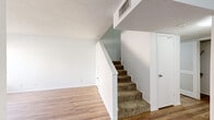 Located at 10330 Gateway Blvd N in El Paso, Texas, this two-story home offers a functional and well-organized layout across two floors. The main level features hardwood-style flooring, a carpeted staircase with white painted railings, and a textured ceiling, creating a clean and neutral aesthetic throughout. A convenient bathroom is also found on this floor. The upper level hosts both bedrooms, each finished with plush carpet and featuring dedicated closets. The spacious primary bedroom benefits from notably tall, vaulted ceilings that enhance the sense of openness, while the second bedroom includes a window with a blind that allows natural light to filter in. Three bathrooms serve the home in total, each equipped with warm wood-toned cabinetry, granite-style countertops, and wide vanity mirrors. One full bathroom on the upper level includes a tiled tub-shower combination with classic white square tile surrounds. Additional storage is provided through three closets distributed across the home. The overall color palette is bright and neutral, with white walls throughout, lending a clean, move-in-ready feel to the entire space.