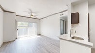 This thoughtfully designed 1-bedroom, 1-bathroom unit offers a comfortable and functional layout across a single floor. The open-concept living and kitchen area forms the heart of the space, featuring light gray wood-look flooring, crown molding, and a ceiling fan that enhances airflow and comfort. A sliding glass door floods the living area with natural light and provides outdoor views, while vertical blinds offer privacy control. The kitchen is defined by rich, dark wood cabinetry, white countertops, a peninsula with a single-basin sink, and stainless steel appliances including a refrigerator, microwave, and range. The bedroom is carpeted for warmth and comfort, equipped with its own ceiling fan, and benefits from multiple windows that invite natural light and outdoor views. Two closets provide ample storage throughout the unit. The bathroom features a full tub-shower combination with white tile surround, complemented by clean, bright finishes. Neutral white walls throughout create a bright, airy ambiance that lends itself well to personalization. The overall design balances practicality with a modern aesthetic, making efficient use of the available space.