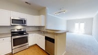 This well-appointed 1-bedroom, 1-bathroom residence is thoughtfully designed to maximize comfort and functionality across a single floor. The open-concept layout seamlessly connects the kitchen and living area, creating a cohesive and airy living environment. The kitchen is outfitted with crisp white cabinetry, granite-style countertops, and a full suite of stainless steel appliances, including an electric range, microwave, and dishwasher. A peninsula countertop extends toward the living space, offering additional prep space and a natural transition between the two areas. Track lighting overhead ensures the kitchen is well-lit for cooking and entertaining. The adjacent living area features plush carpeting, neutral wall tones, and a window that invites natural light to fill the room, contributing to a warm and inviting ambiance. The wood-style flooring in the kitchen contrasts beautifully with the carpeted living space, adding visual interest and definition to each zone. The overall design emphasizes a clean, modern aesthetic with practical finishes throughout, making this a comfortable and move-in-ready home.