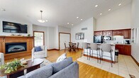 Located at 201 Eaton Ridge Dr in Northfield, Ohio, this single-floor space combines elegant architectural details with a comfortable, open layout. The living room is a standout, boasting soaring vaulted ceilings adorned with pendant lighting and a striking arched window with warm wood trim that floods the room with natural light. A wood-mantled fireplace serves as a focal point, complemented by hardwood flooring and views of the outdoor surroundings through multiple windows. The kitchen is thoughtfully designed with rich cherry wood cabinetry reaching toward the high ceilings, light granite countertops, black appliances including a full-size refrigerator and built-in microwave, and durable tile flooring that transitions seamlessly between the functional spaces. The dining area connects naturally to the living room through an elegant arched passageway, featuring the same warm hardwood floors, a glass-top dining table, and a set of double doors that open to additional spaces. Throughout the space, consistent warm wood trim, soft neutral wall tones, and abundant natural light from multiple windows create a cohesive, inviting ambiance that balances style and practicality.