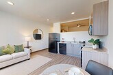 Located in Aurora, CO, this well-designed one-bedroom, one-bathroom unit makes smart use of its compact footprint across a single floor. The entry hallway sets a clean, organized tone, featuring a built-in coat hook rail and a small bench — a practical mudroom-style introduction to the home. Light wood-tone luxury vinyl flooring flows consistently throughout the entire unit, lending warmth and visual continuity.

The heart of the unit is an open-concept great room combining the living, dining, and kitchen areas. The kitchen is outfitted with light wood cabinetry, granite-style countertops, and black appliances including a refrigerator, dishwasher, electric range, and over-the-range microwave. A ceiling fan overhead adds comfort to the space. The living area offers a bright, airy atmosphere with large windows that bring in ample natural light and outdoor views of surrounding greenery.

The private bedroom is a comfortable and well-lit retreat, featuring dual windows with vertical blinds and a wall-mounted HVAC unit. The combined bathroom and laundry room is clean and functional, featuring a full soaking tub with shower and crisp white finishes. Every element of this unit is designed to maximize efficiency without sacrificing comfort or style.