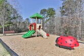 Located in Columbus, Georgia (31904), this single-level outdoor community space offers a welcoming environment surrounded by natural beauty. The grounds are characterized by gently sloping grassy areas that transition into a backdrop of tall pines and mixed deciduous trees, providing a natural buffer and a sense of privacy throughout the property.

A standout feature of this space is the dedicated playground area, equipped with a multi-level play structure complete with slides, a covered tower, and interactive elements, all set within a wood chip safety surface bordered by timber edging. This makes the area well-suited for families with children.

Concrete walkways wind through the property, providing smooth and accessible pathways connecting the various areas of the community. The well-maintained grounds include open lawn spaces that offer room for outdoor activities and relaxation. Neighboring residential buildings are visible in the background, reinforcing the community-oriented character of the space.

The mature tree line along the perimeter not only adds to the aesthetic appeal but also provides natural shade and a serene, park-like ambiance. Under clear blue skies, the combination of open green space, wooded edges, and community amenities creates an inviting outdoor environment for residents of this Columbus, GA neighborhood.