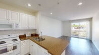 This single-story unit offers a thoughtfully organized floor plan that makes efficient use of its space. The combined kitchen and living area forms the heart of the unit, where an open-concept layout promotes a sense of spaciousness and connectivity. The kitchen is well-appointed with white raised-panel cabinetry extending to the ceiling, warm granite-style countertops, a peninsula with an integrated double stainless steel sink, and white appliances including a refrigerator, electric range, microwave, and dishwasher. Recessed lighting illuminates the kitchen, while the living area benefits from natural light streaming through a sliding glass door that opens to a private balcony with views of surrounding greenery and rooftops.

Dark hardwood-style flooring runs consistently throughout the unit, providing a cohesive, modern aesthetic against the clean white walls. The bedroom is a comfortable size, featuring a window with outdoor views, a closet for dedicated storage, and the same flooring. The bathroom maintains the unit's clean design language with white cabinetry, a large vanity mirror, a single-sink vanity, and a shower-tub combination. Two hallways connect the spaces efficiently, completing a practical and well-organized layout.